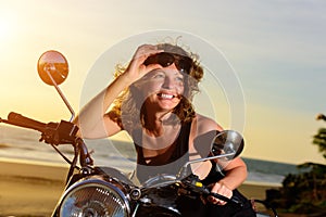 Portrait of a beautiful woman sitting on motorcycle, smiling and holding sunglasses on the forehead