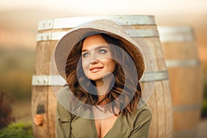 Portrait of beautiful woman smiling with curly hair in hat enjoying at park  by wooden barrel. Autumn Sunset photo