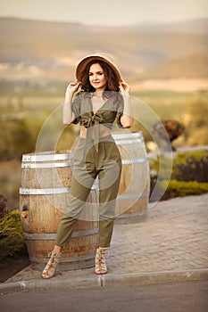 Portrait of beautiful woman smiling with curly hair in hat enjoying at park  by wooden barrel. Autumn Sunset photo