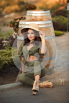 Portrait of beautiful woman smiling with curly hair in hat sitting by wooden barrel at park. Autumn Sunset photo