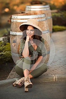 Portrait of beautiful woman smiling with curly hair in hat sitting by wooden barrel at park. Autumn Sunset photo