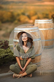 Portrait of beautiful woman smiling with curly hair in hat sitting by wooden barrel at park. Autumn Sunset photo