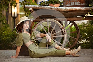 Portrait of beautiful woman smiling with hat enjoying at park. Attractive brunette with curly hair sitting by wooden cart with