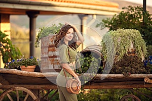 Portrait of beautiful woman smiling with round straw bag enjoying at park  by wooden cart with green grass and flowers. Sunset