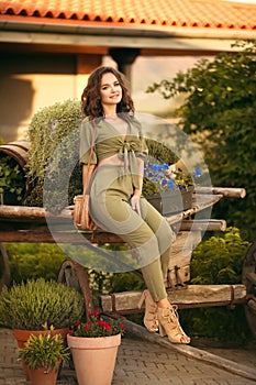 Portrait of beautiful woman smiling with round straw bag enjoying at park  by wooden cart with green grass and flowers. Sunset