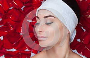 Portrait of a beautiful woman in a spa salon in front of a beauty treatment against the background of red rose petals.