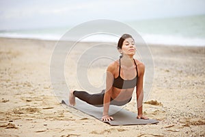 A portrait of beautiful woman standing in plank position and stretching her back on the beach.