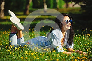 Portrait of beautiful woman in sunglasses lying on summer green grass with bright colors. Joyful girl wears bright