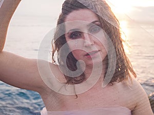 portrait of beautiful woman through a transparent tulle fabric on the seashore at sunset. No retouching, no plastic