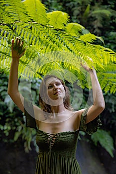 Portrait of beautiful woman under the fern leaves. Caucasian woman wearing green dress walking in tropical jungle. Nature concept