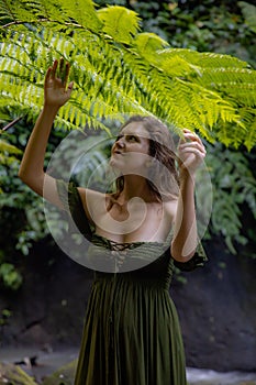 Portrait of beautiful woman under the fern leaves. Caucasian woman wearing green dress walking in tropical jungle. Nature concept