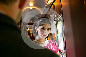 Portrait of beautiful woman in vintage dress standing in corridor of locomotive train with officer in uniform watching