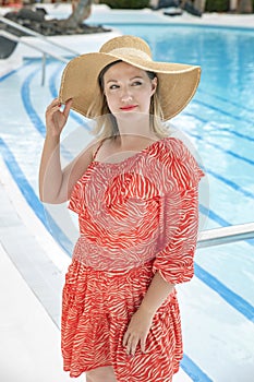 Portrait of a beautiful woman wearing a casual red summer dress and a fashionable oversized straw hat