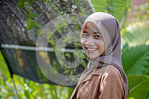 portrait of a beautiful woman wearing a modern hijab on the side of the greenhouse with a sweet smile and negative space left