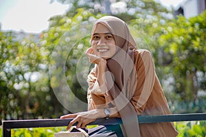 portrait of a beautiful woman wearing a modern hijab sitting with her hand on her chin and smiling sweetly