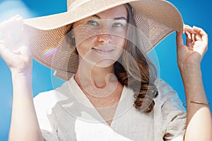 Portrait of beautiful woman wearing straw hat with large brim  looking at camera. Closeup face  smiling girl with freckles and