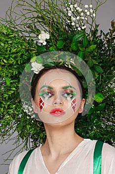 Portrait of a beautiful woman in a white dress with a green ribbon and with branches on her head. Creative makeup