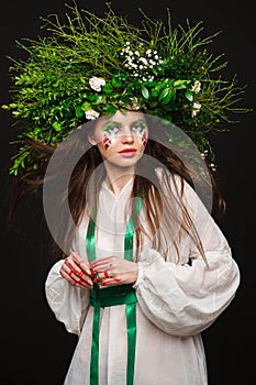 Portrait of a beautiful woman in a white dress with a green ribbon and with branches on her head. Creative makeup