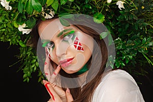 Portrait of a beautiful woman in a white dress with a green ribbon and with branches on her head. Creative makeup