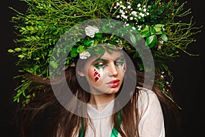 Portrait of a beautiful woman in a white dress with a green ribbon and with branches on her head. Creative makeup