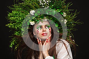 Portrait of a beautiful woman in a white dress with a green ribbon and with branches on her head. Creative makeup