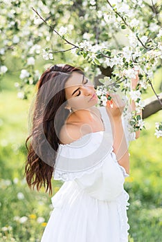 Portrait of a beautiful woman in a white dress in a spring garden. A girl with her eyes closed inhales the fragrance of flowering