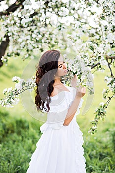 Portrait of a beautiful woman in a white dress in a spring garden. The girl inhales the fragrance of flowering trees