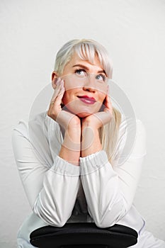 Portrait of a beautiful woman in a white suit on a light background. A gesture of daydreaming, planning, thinking and