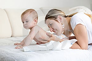 Portrait of beautiful young woman caressing and looking at her baby son lying on bed