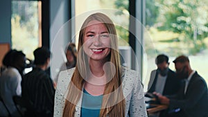 Portrait of beautiful young 30s blonde business woman smiling at camera at modern light office background slow motion.