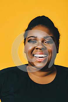 portrait of a beautiful young adult african american woman laughing with afro hairstyle on yellow background