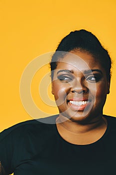 portrait of a beautiful young adult african american woman smiling with afro hairstyle on yellow background