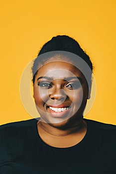 portrait of a beautiful young adult african american woman smiling with afro hairstyle on yellow background