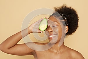 Portrait of a beautiful young African woman holding an avocado and smiling against a beige background. The concept of