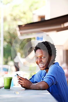 Beautiful young african woman relaxing at outdoor cafe with a smart phone