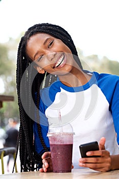 Beautiful young african woman sitting at cafe with mobile phone and drink