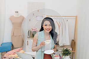 Portrait of beautiful young Asian fashion designer businesswoman at her studio while drinking coffee
