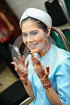 Portrait of beautiful young Asian female model smiling and showing hands with henna tattoo after make up by professional artist