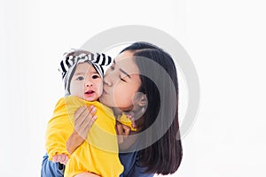 Mother kissing her infant newborn baby in a white bed