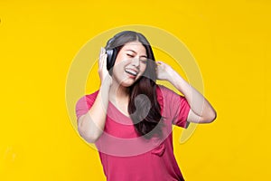 Portrait of beautiful young asian woman dancing and listening to music having fun in summer on yellow background