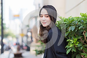 Portrait of a beautiful young Asian woman in long hair wearing a black coat standing smiling happy outdoors in the city