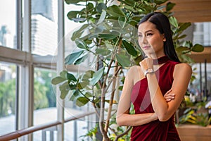 portrait of Beautiful young asian woman in red dress standing and looking out the window . elegant lady model positive thinking