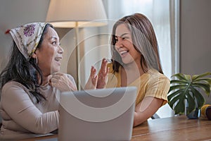 Portrait of a beautiful young Asian woman smiling and hugging her middle aged mom or grandmother, spending time at home