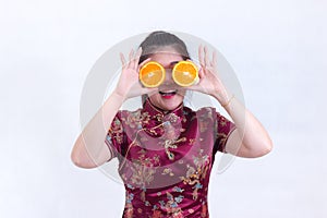 Portrait of Beautiful Young asian woman wear chinese dress traditional cheongsam or qipao. holding orange slices front of her eye