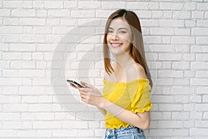 Portrait of beautiful young Asian woman wear yellow off-shoulders clothes holding smartphone, standing and looking at camera white