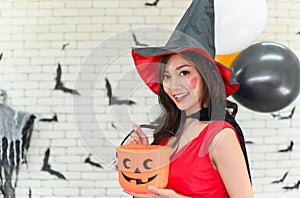 Portrait of beautiful young asian woman wearing witch costume posing with balloons on background decorated for halloween party -