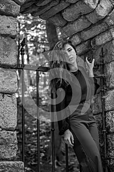 Portrait of a beautiful young and attractive teen girl with long hair near the steel gates of the destroyed stone castle in