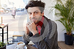 Portrait of beautiful young bearded brunette man looking positively at camera with charming smile and leaning his head on raised