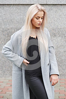 Portrait of a beautiful young blond woman in grey coat and black leather pants. Street fashion look
