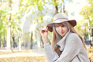 Portrait of a beautiful young blond woman with shiny straight hair in a brown hat in the park